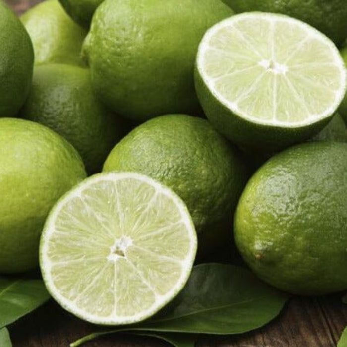 Green limes with one cut in half on a wooden surface