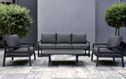 Outdoor furniture set with gray sofa and chairs on a stone patio against a gray wall.