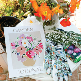Garden journal, gloves, and shoes on a brick surface with flowers in the background