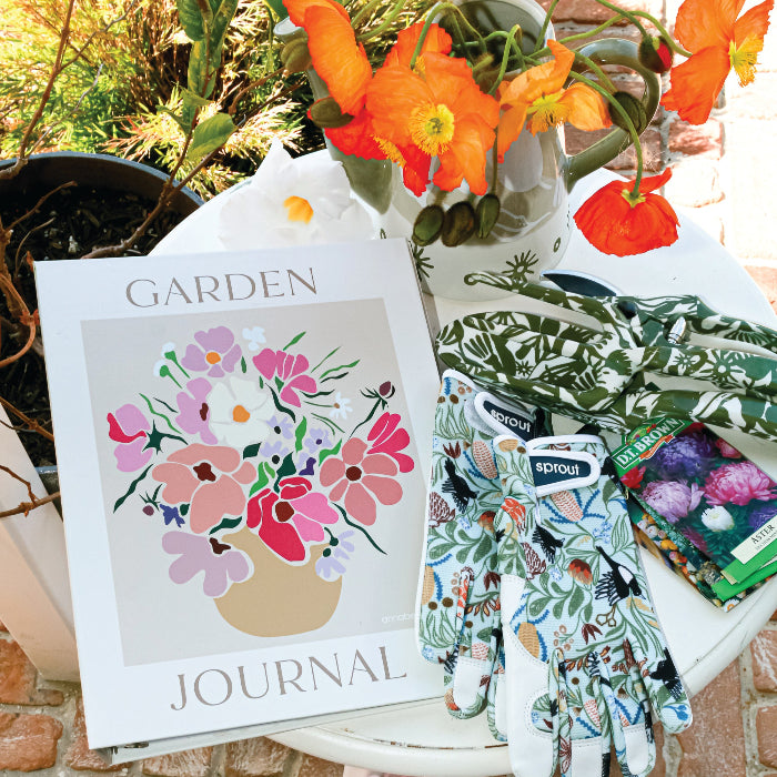 Garden journal, gloves, and shoes on a brick surface with flowers in the background