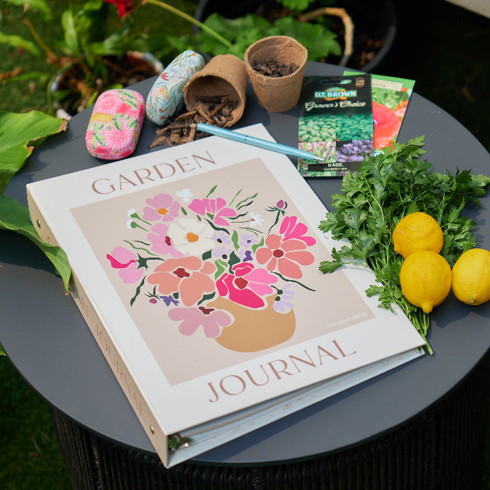 Garden journal with floral design on a table outdoors, surrounded by plants and lemons.