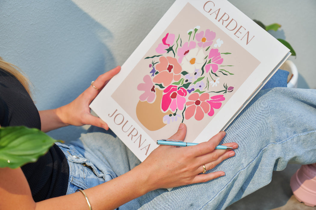Person holding a 'Garden Journal' book with floral design on a light blue couch.