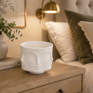 White ceramic face-shaped candle holder on a wooden surface with a cozy indoor setting.