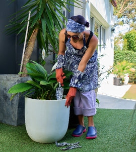 Person gardening with tools near a large potted plant in a garden setting