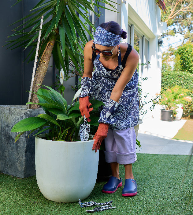 Person gardening with tools near a large potted plant in a garden setting