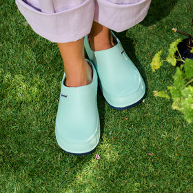 Person wearing light blue rain boots on grass next to a plant