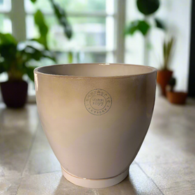 Beige planter with a logo on a gray surface, with decorative items in the background.
