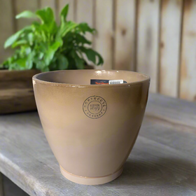 Beige ceramic planter with a logo on a beige surface, with decorative items in the background.