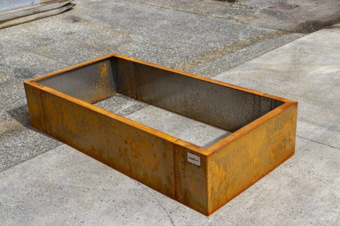 Rust-colored metal planter box on a concrete surface