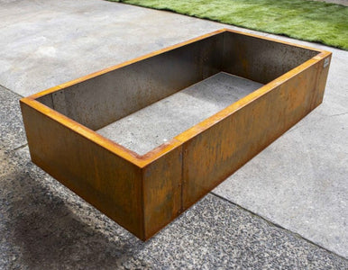 Corten steel fire pit on a concrete surface with grass in the background