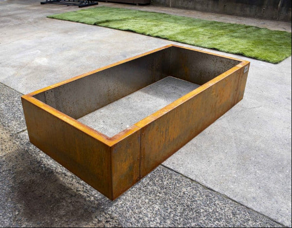 Corten steel fire pit on a concrete surface with grass in the background