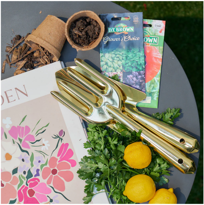 Gold gardening tools on a table with seeds, soil, and lemons