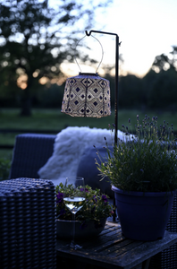 Outdoor setting with a lantern, potted plant, and glass on a table at dusk.