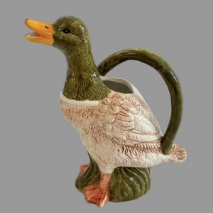 A ceramic duck-shaped pitcher with a green head and handle, a cream-colored body with pinkish feather detailing, and an orange beak, shown against a plain light background.