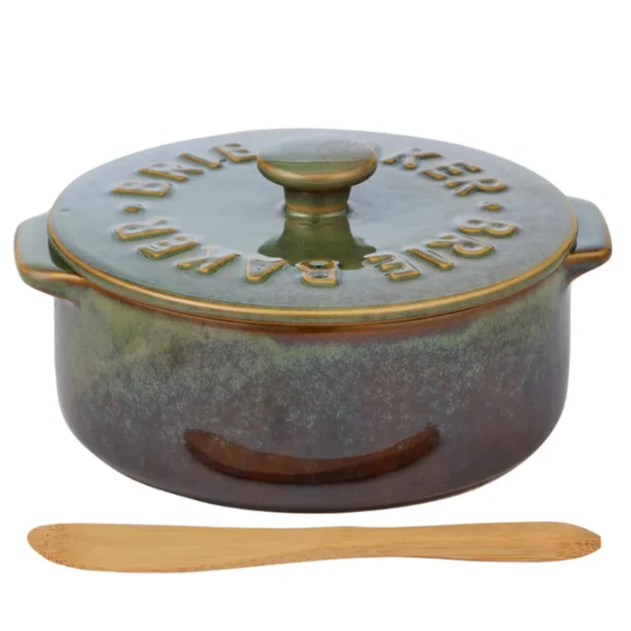 A round ceramic Dutch oven pot with a matching lid, featuring embossed text reading 'JULE KERR BAE RAVN' around the lid rim, shown with a wooden spoon below on a white background.