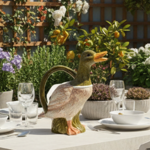 A ceramic duck-shaped pitcher with a green head and handle, a cream-colored body with pinkish feather detailing, and an orange beak, shown against a plain light background.