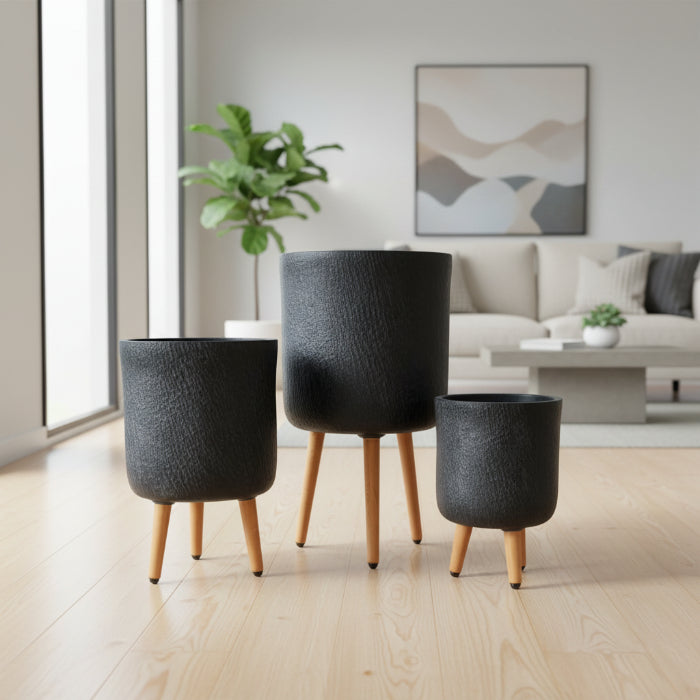Three black textured planters with wooden legs against a brick wall.