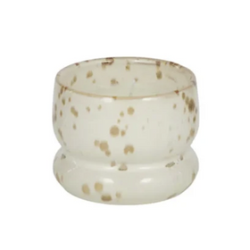 A small round glass candle holder or candle cup with a flared base, featuring a speckled pattern of light brown and beige dots on a translucent off-white glass background, isolated on a white background.