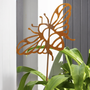 Rust-colored bee-shaped garden stake on a plant with a neutral background