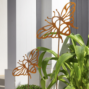 Metal butterfly decorations on stakes with a plant in the foreground.