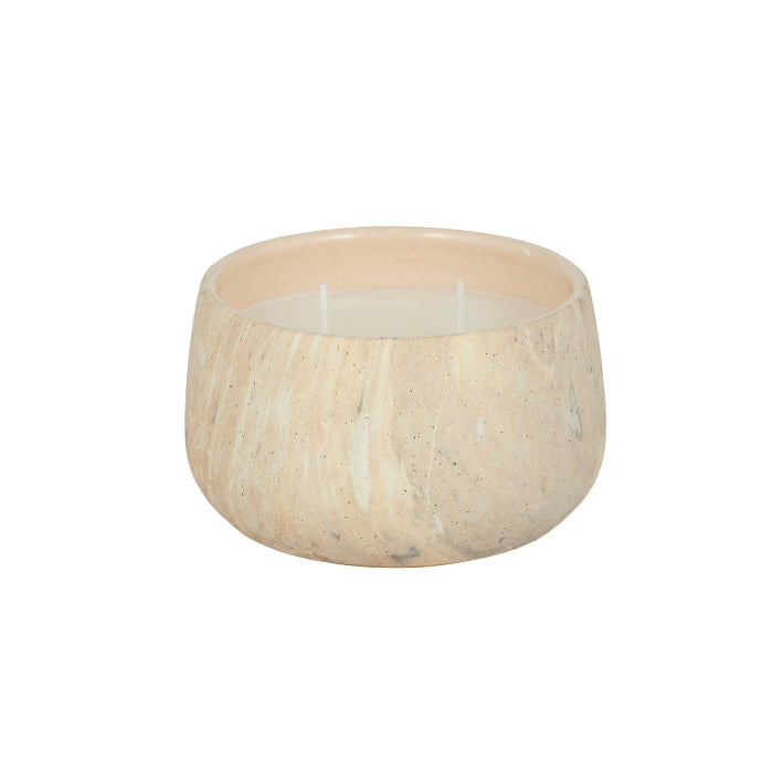 A two-wick candle in a round, organic-shaped vessel made of a light beige stone or marble with subtle natural veining, set against a plain white background.