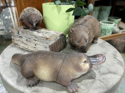 Three animal figurines on a round stone surface with plants in the background