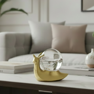 A decorative snail figurine with a polished gold body and a clear glass shell on a plain white background.
