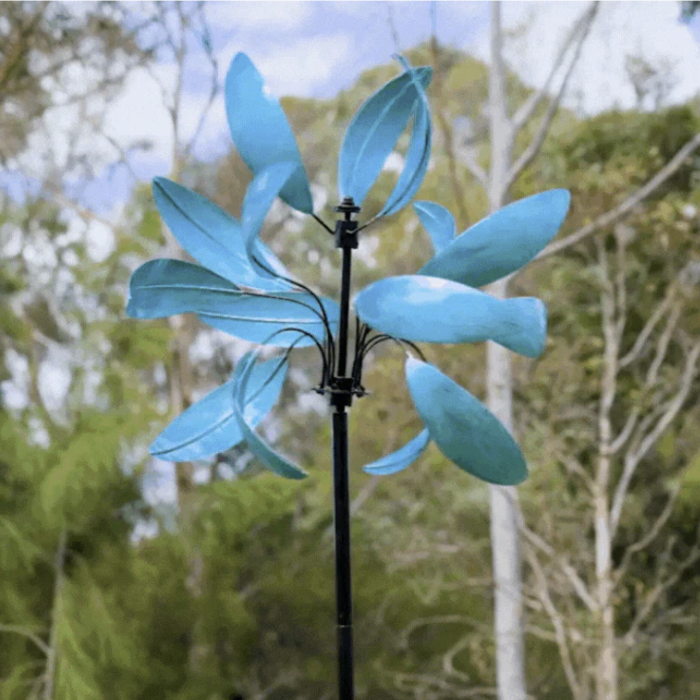 Blue windmill sculpture against a natural background with trees.