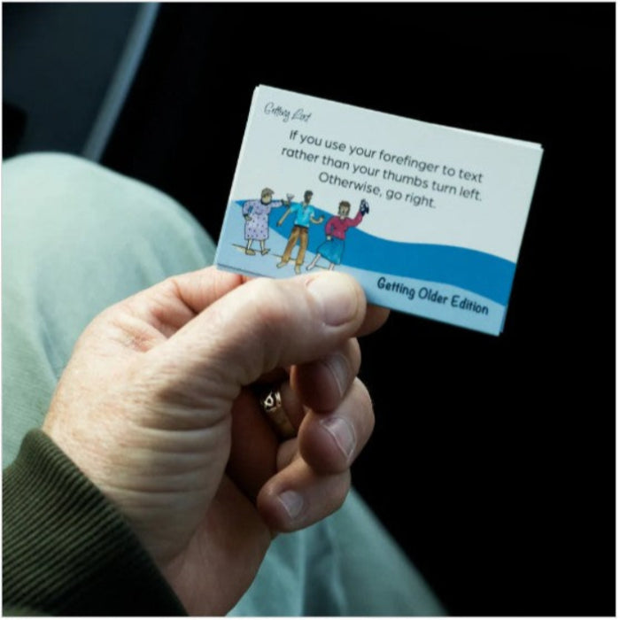 Hand holding a card with humorous text and illustrations, sitting on a dark surface.