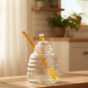 Clear glass honey jar with a yellow dipper on a white background