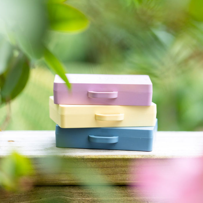 Stack of three colorful boxes on a wooden surface with a blurred green outdoor background