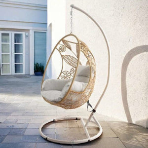 Woven egg-shaped hanging chair with white cushions on a stand outdoors.