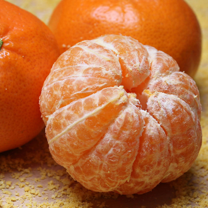 Two oranges, one whole and one peeled, on a textured surface.