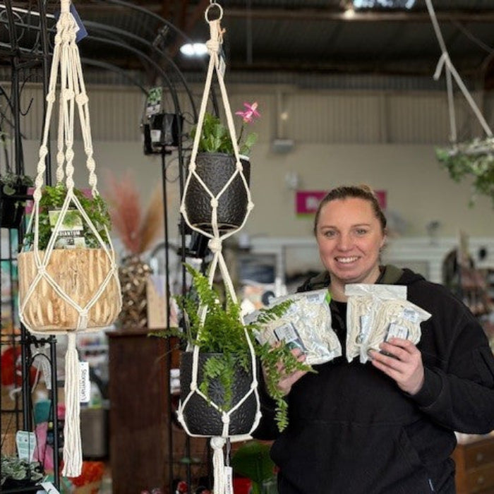 Person holding packages next to macrame plant hangers in a store setting