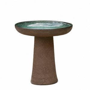 A rustic pedestal bird bath with a textured brown footed base and a shallow, wide round tray featuring a glossy green glazed interior, shown against a plain white background.