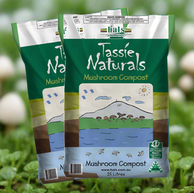 Two bags of Tassie Naturals Mushroom Compost, each with an illustration of mushrooms and a landscape on the front, placed on a bed of greenery with more mushrooms visible in the background.