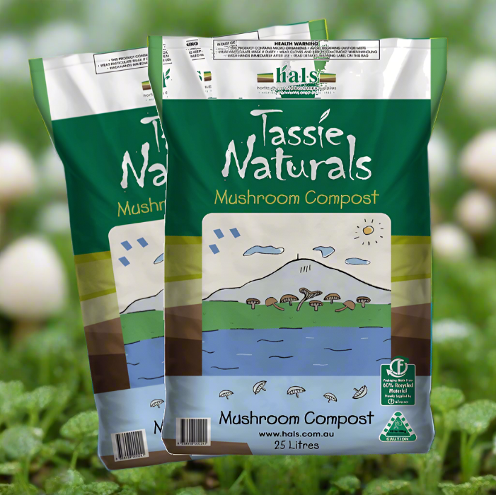 Two bags of Tassie Naturals Mushroom Compost, each with an illustration of mushrooms and a landscape on the front, placed on a bed of greenery with more mushrooms visible in the background.