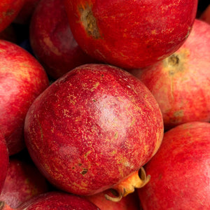 A close-up pile of red pomegranates with textured, speckled skins filling the frame.