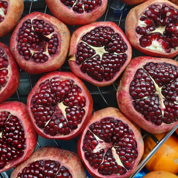 A close-up overhead view of multiple pomegranates, many cut in half to show the deep red arils and pale pith, arranged on a metal rack.