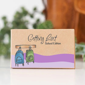 Cardboard box with 'Getting Lost School Edition' text and backpack illustrations on a blurred background
