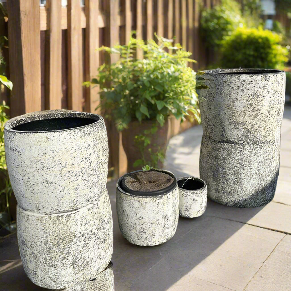 Set of stone-textured planters on a reflective surface with a blurred natural background