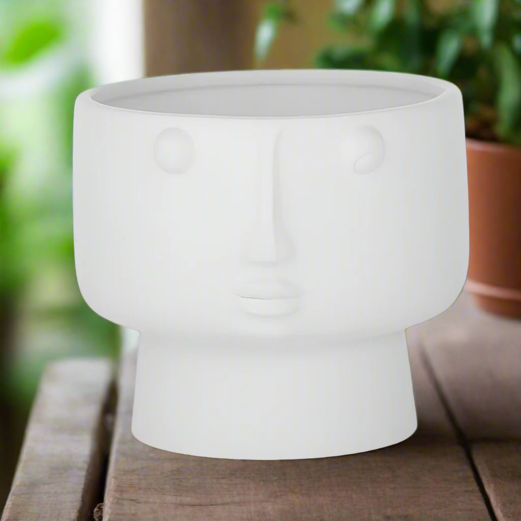 A matte white ceramic pot in the shape of a human head with eyes and a mouth, resembling a classical statue.