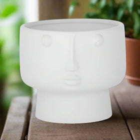 A matte white ceramic pot in the shape of a human head with eyes and a mouth, resembling a classical statue.