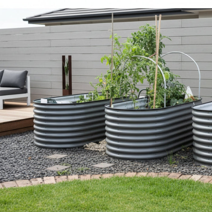 A set of three silver-colored metal raised garden beds placed outdoors, with plants growing in them.