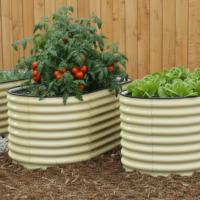 A set of metallic, likely aluminum or steel, raised garden beds placed on a brick pathway with a fence and various plants in the background.